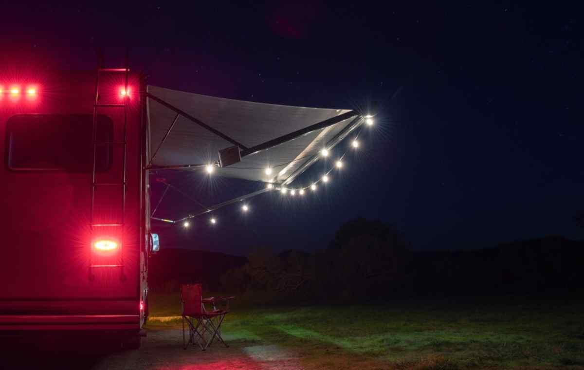 Belle carte postale montrant un camping-car garé dans une forêt pendant une nuit étoilée, avec ses lumières intérieures allumées.