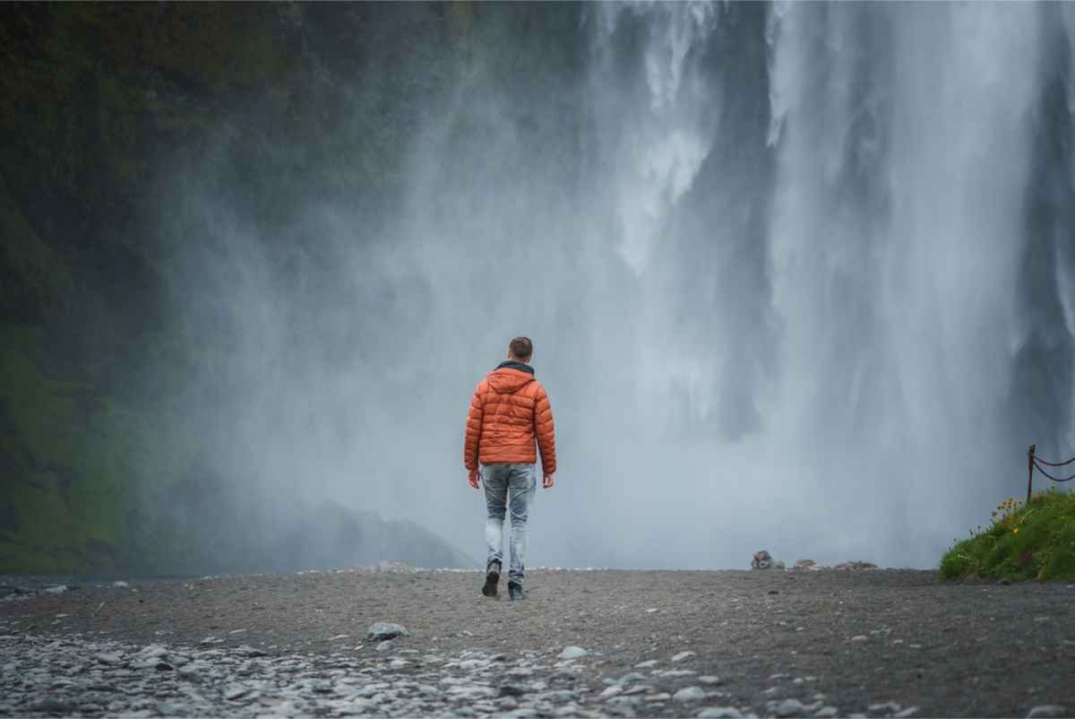 Toourist walking up to a mist of a waterfall in Iceland