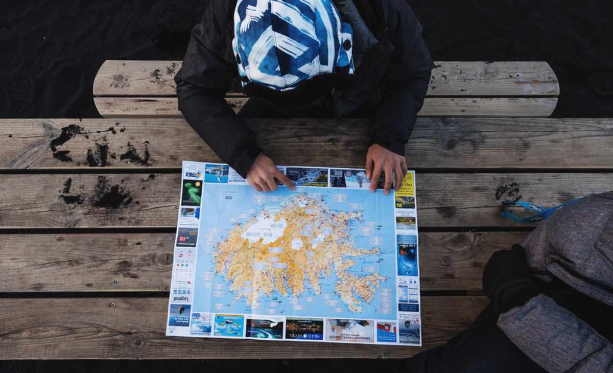 Voyageur assis sur un banc, étudiant une carte détaillée de l’Islande pour préparer le voyage.