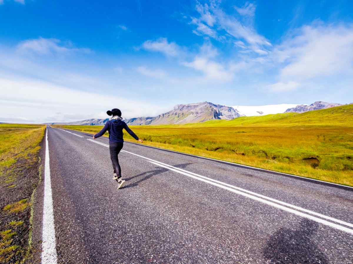 The freedom of driving in Iceland Traveler enjoying the freedom of an empty Icelandic road in summer, with mountains, blue skies, and wide open landscapes.