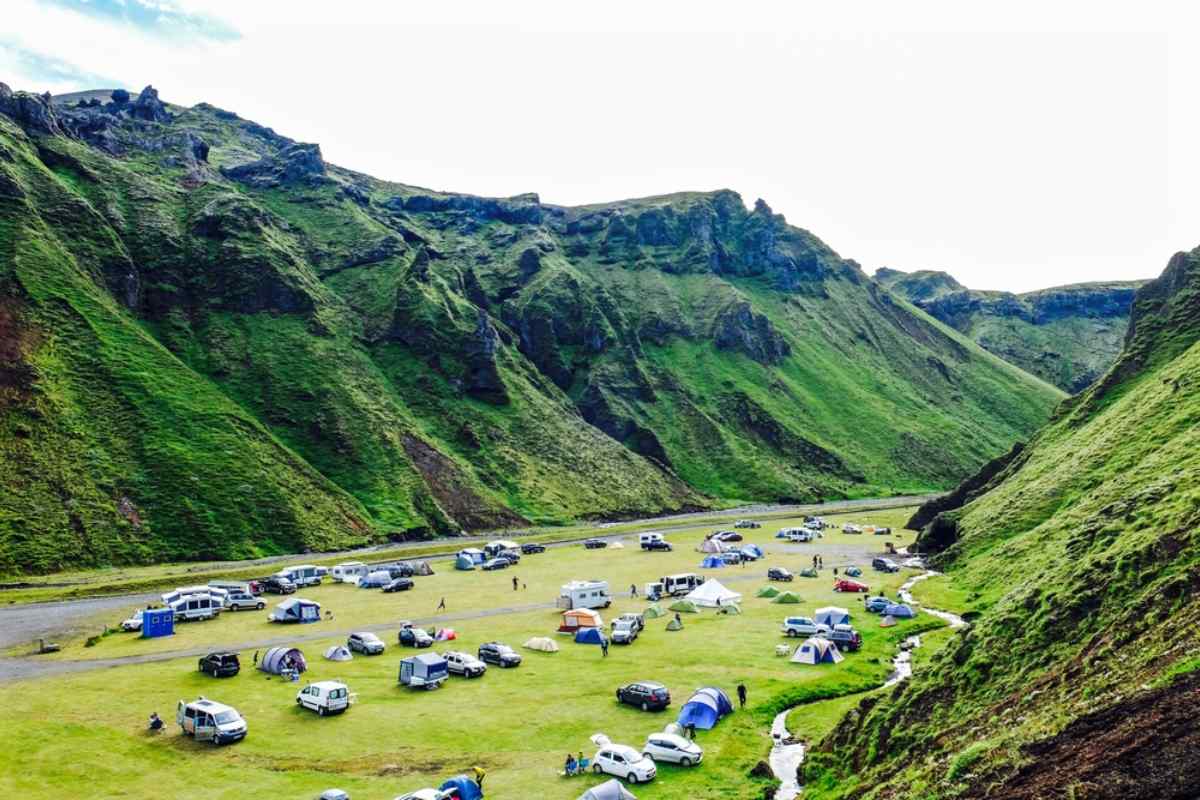 Camping-car longeant une route côtière avec des montagnes imposantes et un ciel bleu d’été, illustrant la liberté d’explorer des paysages isolés en vé