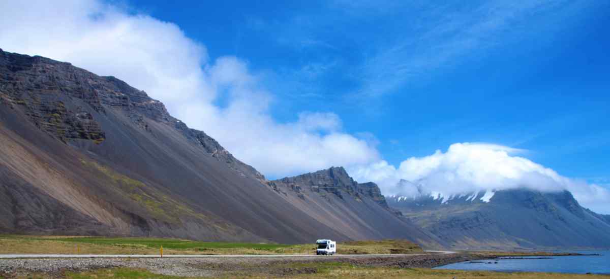 Wohnmobil auf einer Küstenstraße mit dramatischen Bergen und blauem Sommerhimmel – ein Bild der Freiheit, Islands abgelegene Landschaften mit einem Ca