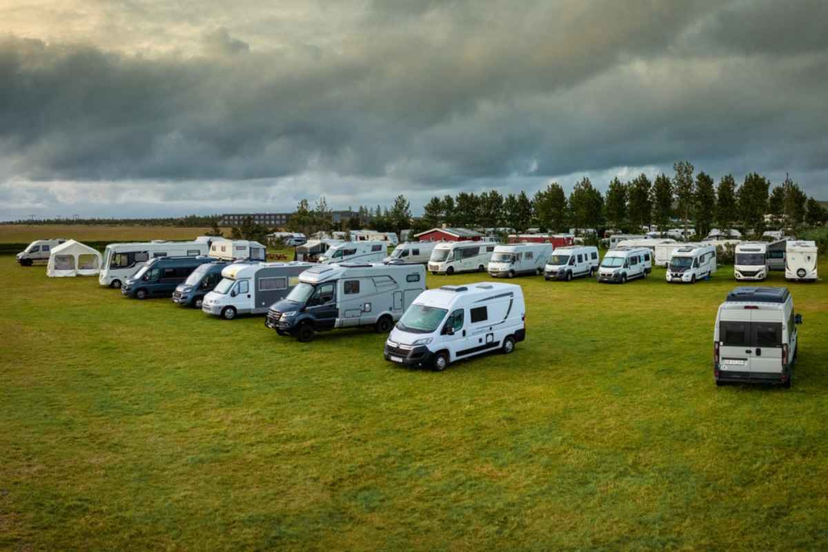 Campervans and motorhomes parked in a large grassy Iceland campsite under dark cloudy skies