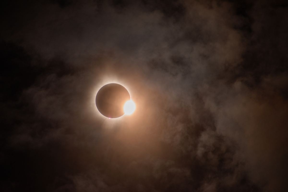 Partial solar eclipse glowing through dark clouds in the sky