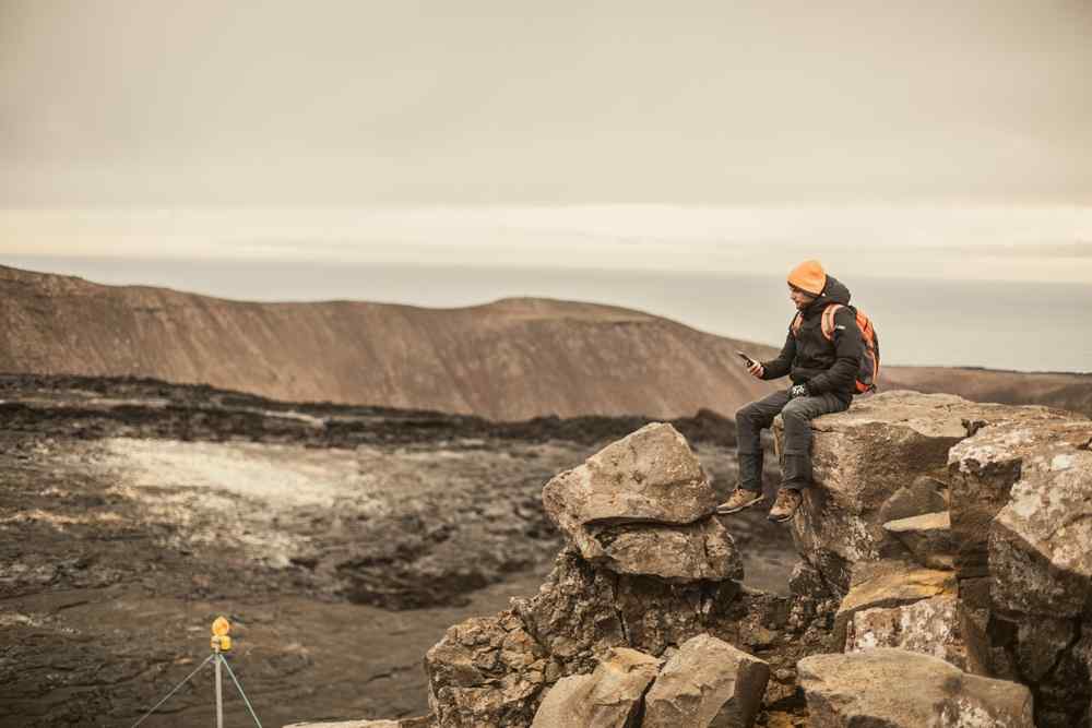 Lack of connectivity in Iceland Traveler sitting on rocks and checking a phone in a rugged volcanic landscape in Iceland.
