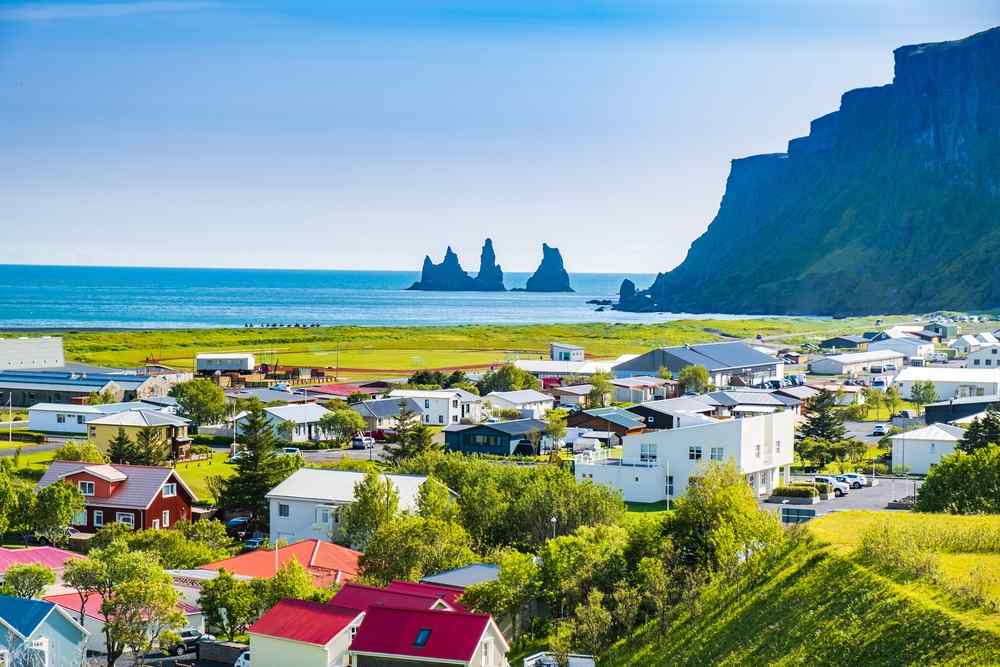 Iceland's Vík Coastal view of Vík in South Iceland with colorful houses, green fields, steep cliffs and the Reynisdrangar sea stacks offshore.