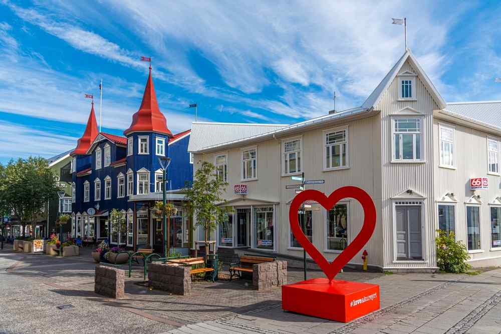 Iceland's Akureyri Colorful historic buildings and the red Akureyri heart sculpture in the city center beneath a bright blue Icelandic sky.