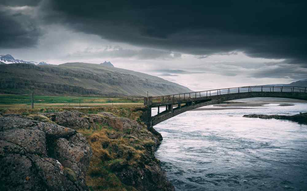 Iceland's Eastfjords Bridge crossing a river in Iceland’s Eastfjords, surrounded by rugged mountains and dramatic storm clouds.
