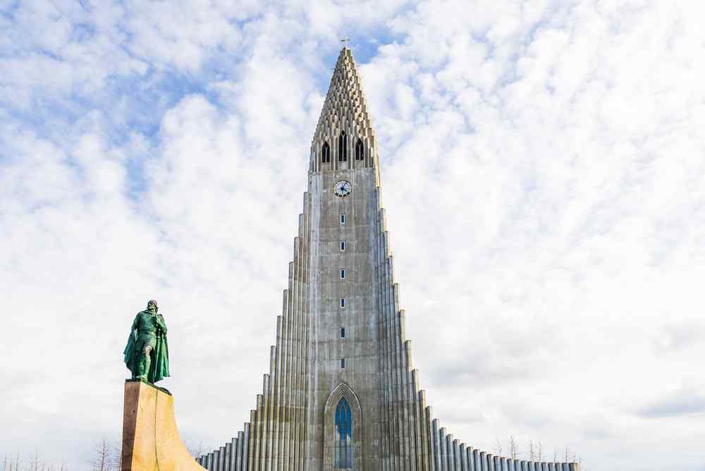 Hallgrímskirkja in Reykjavík Hallgrímskirkja church and the Leif Erikson statue in Reykjavík beneath a bright sky filled with scattered clouds.
