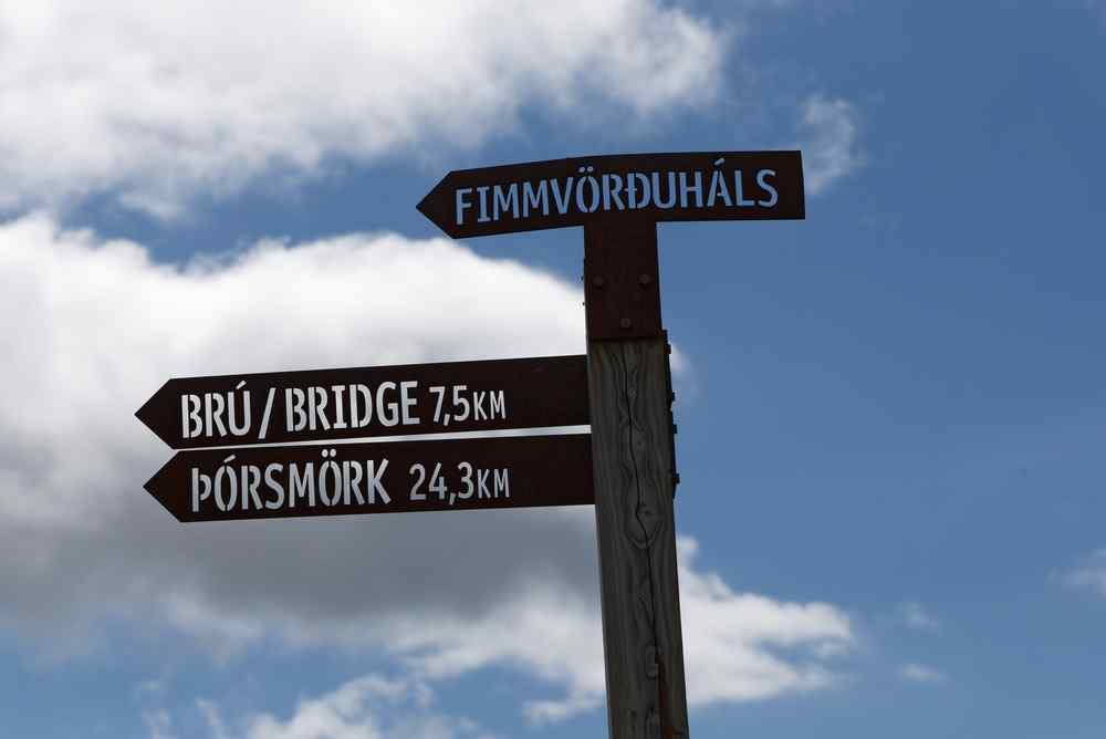 Þórsmörk hiking sign Hiking sign in Iceland pointing toward Fimmvörðuháls, Brú Bridge and Þórsmörk beneath a blue and cloudy sky.