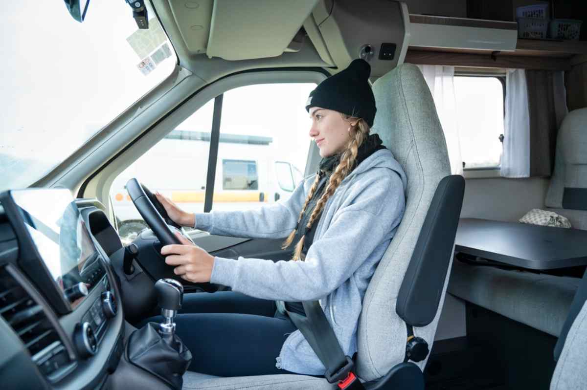 Traffic rules in Iceland Young woman at the wheel of a motorhome, wearing a beanie and seatbelt, focused on driving inside the camper’s bright, modern cabin.