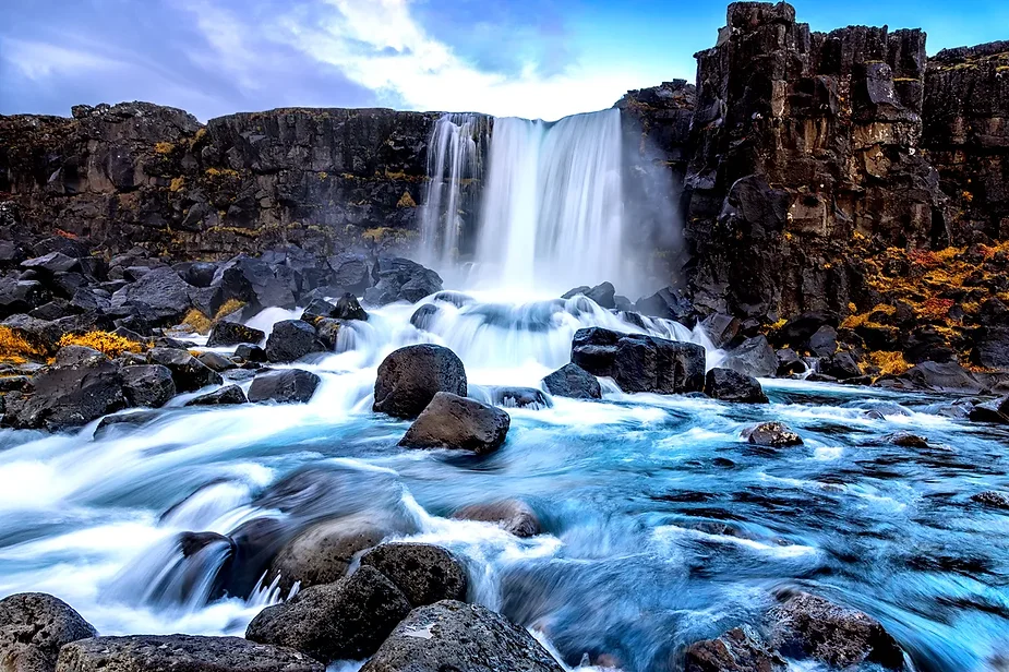 A powerful view of Öxarárfoss Waterfall flowing over volcanic rocks, with blue water rushing downstream in Thingvellir National Park, Iceland.