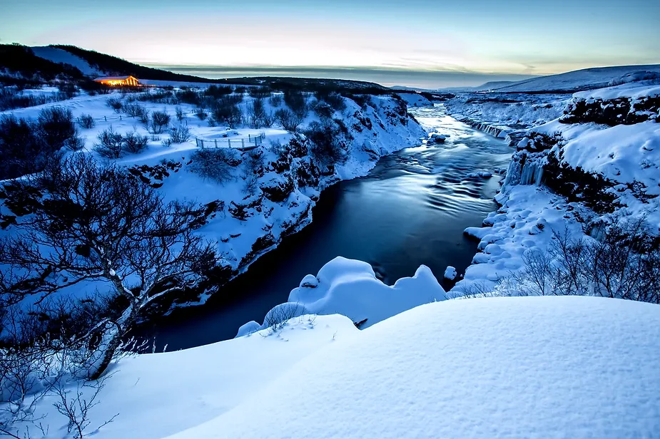 Winter view of Hraunfossar waterfall in Iceland, with snow-covered landscape and icy river under a twilight sky