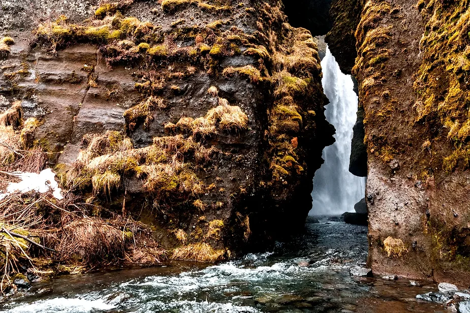 Close-up view of Gljúfrabúi Waterfall in Iceland, cascading through a narrow opening between moss-covered cliffs, with a stream flowing in the foreground.