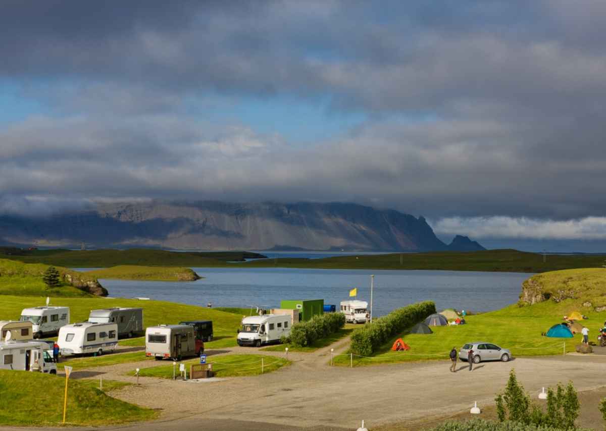 Campervans and tents at a campsite near H&ouml;fn with mountains and water in the background.