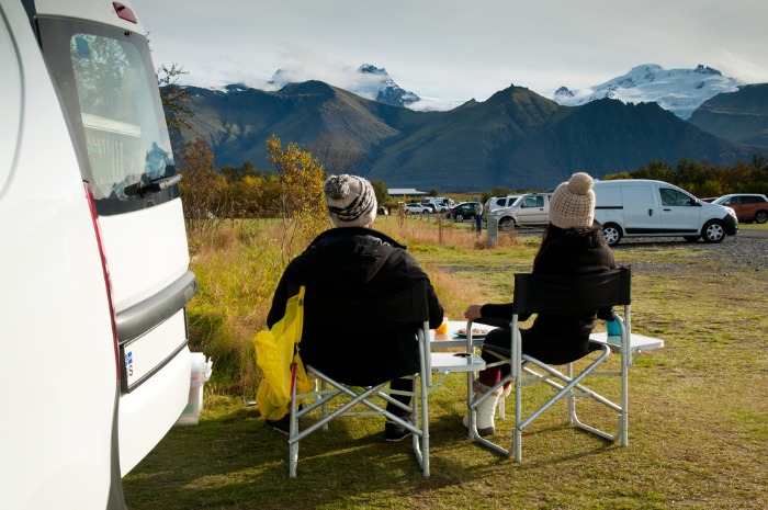 A couple having their meal on a campsite in Iceland with their rented campervan, looking at the picturesqua landscape