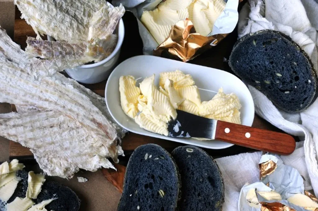 Traditional Icelandic snack with dried fish, butter, and slices of black rye bread, arranged on a wooden board, representing a typical local delicacy