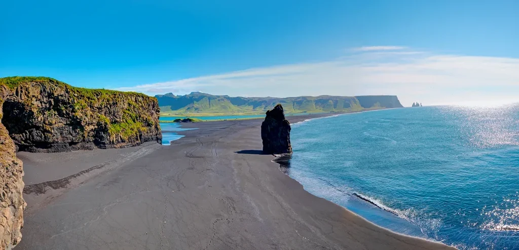 Una vista panoramica della spiaggia di Reynisfjara in Islanda, con sabbia nera, scogliere rocciose, formazioni rocciose marine in lontananza e montagn