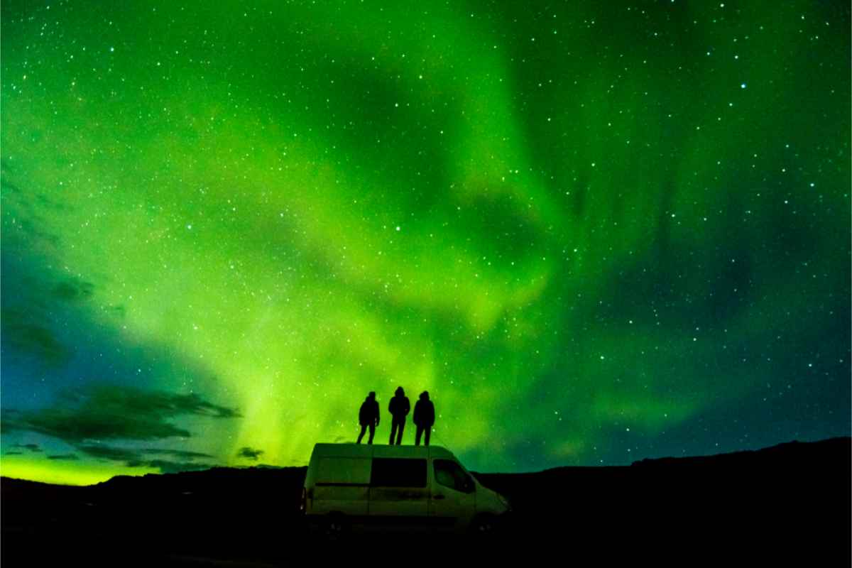Tourists watching the Northern Lights from the top of their campervan rental