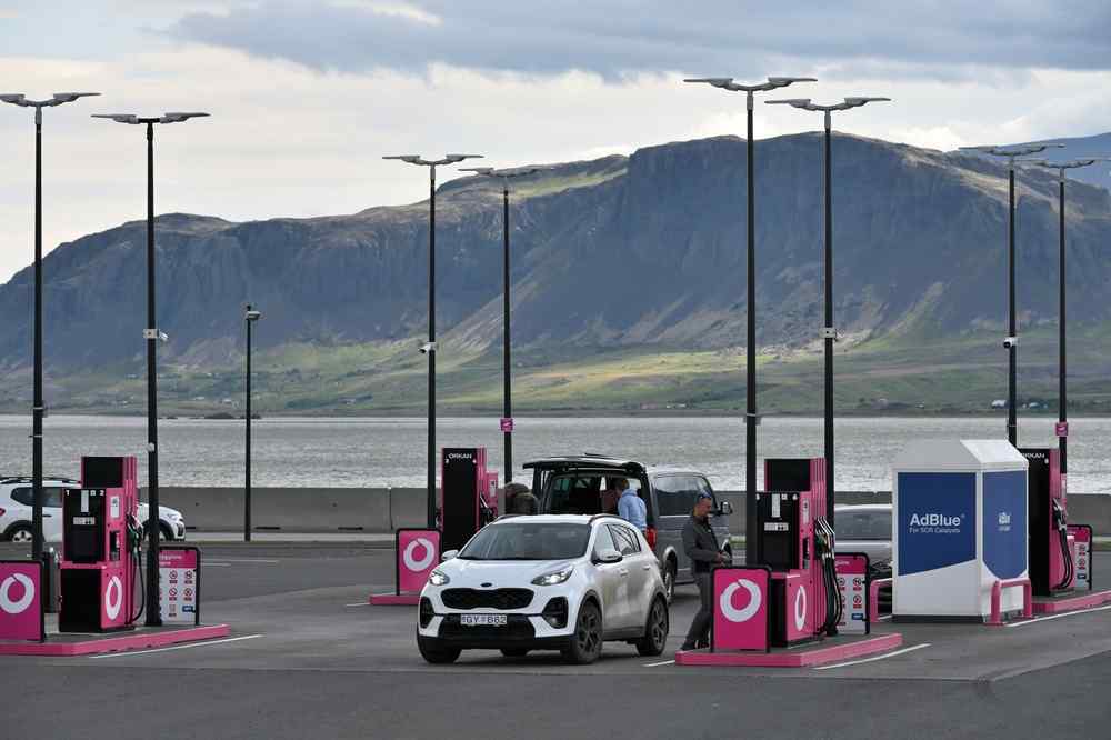Tankstelle in Island Autos beim Tanken an einer Tankstelle in Island mit Bergen auf der anderen Seite des Wassers.