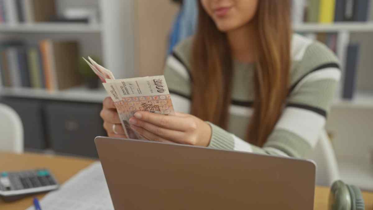 Frau zählt isländische Kronen an einem Schreibtisch mit Laptop.