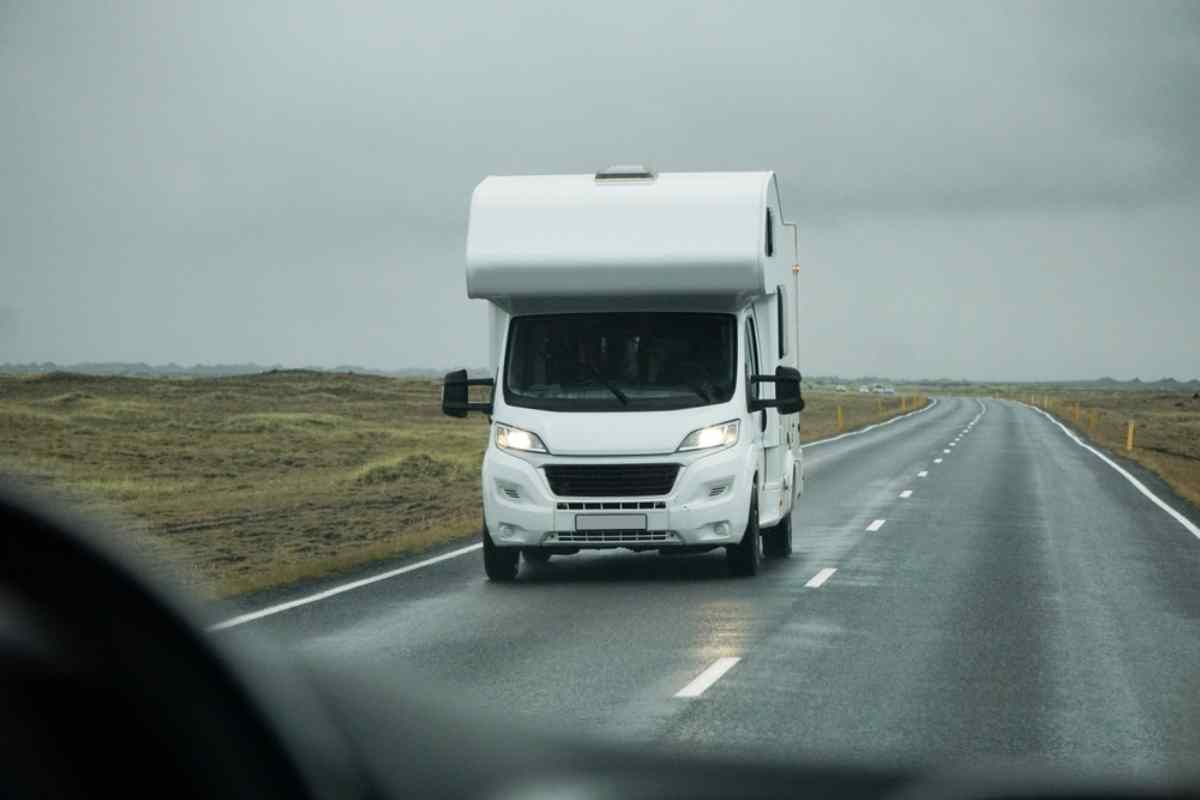 Weißer Campervan fährt auf einer leeren Straße durch isländische Landschaften.