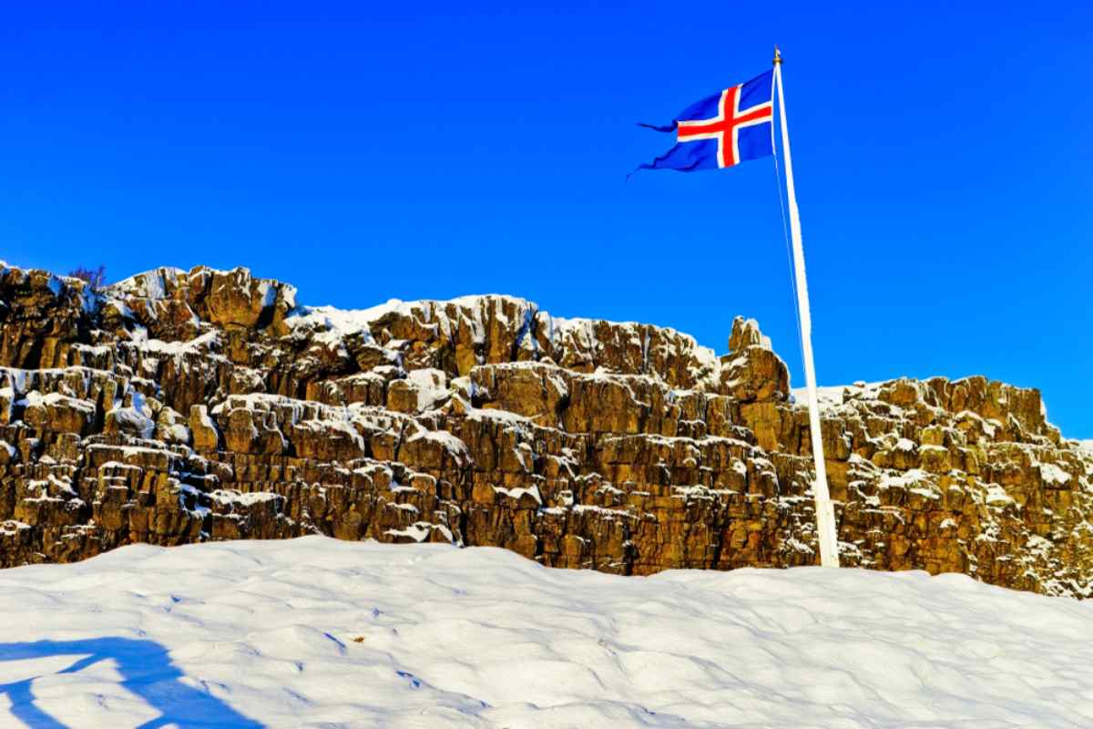 Isländische Flagge in Þingvellir Isländische Flagge weht über verschneiten Klippen im Nationalpark Þingvellir.