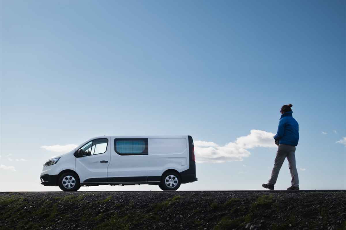 Tourist geht direkt an seinem weißen Campervan an einem sonnigen Tag vorbei
