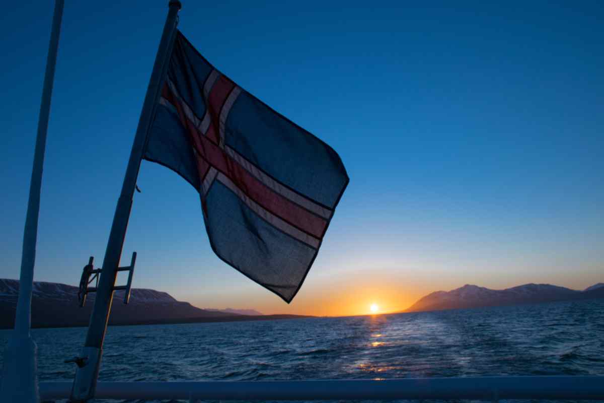 Wann nach Island reisen? Isländische Flagge auf einem Boot bei Sonnenuntergang über einem nördlichen Fjord.