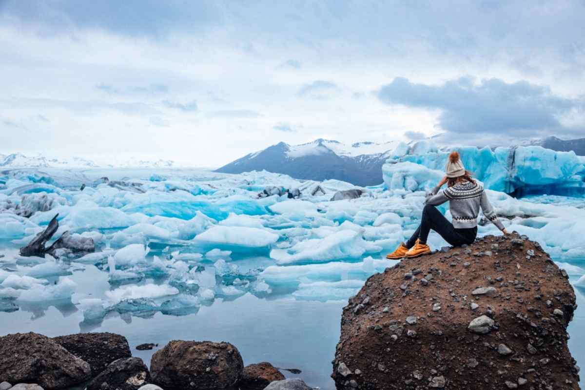 Jökulsárlón in Island Reisende sitzt auf einem Felsblock mit Blick auf blaue Eisberge in der Lagune Jökulsárlón.