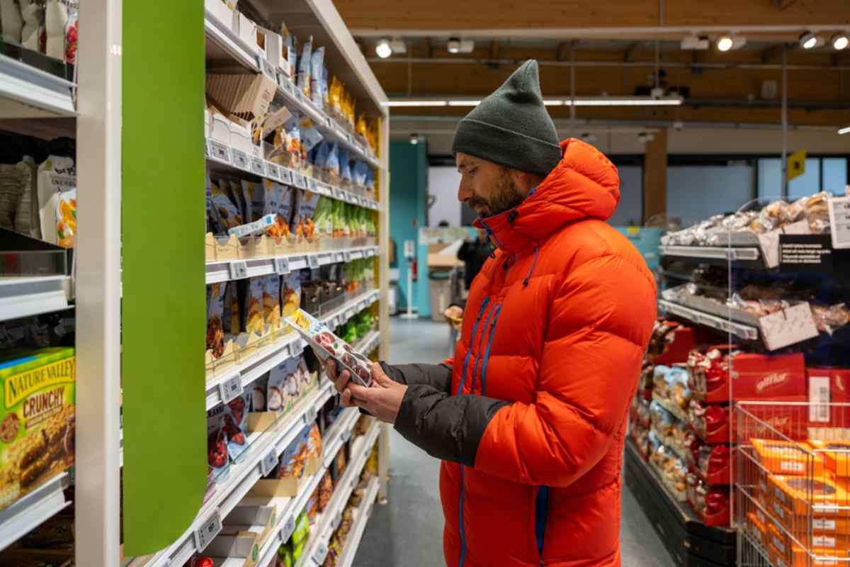 Lebensmittel in Island kaufen Kundin im Steppmantel vergleicht Snacks im Gang eines isländischen Supermarkts.