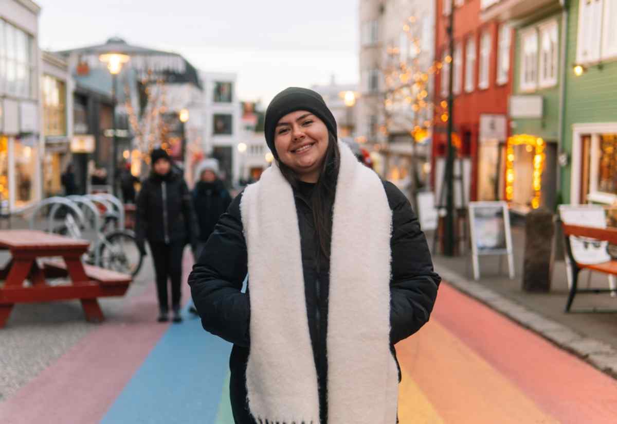Ist Island ein sicheres Land? Lächelnde Reisende auf Reykjavíks Regenbogenstraße während Winterlichtern und Dekorationen.