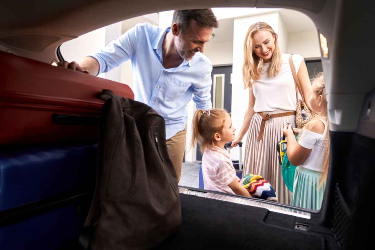 Familie, die bunte Koffer in den Kofferraum des Autos l&auml;dt, bevor sie zu einem Roadtrip aufbricht.