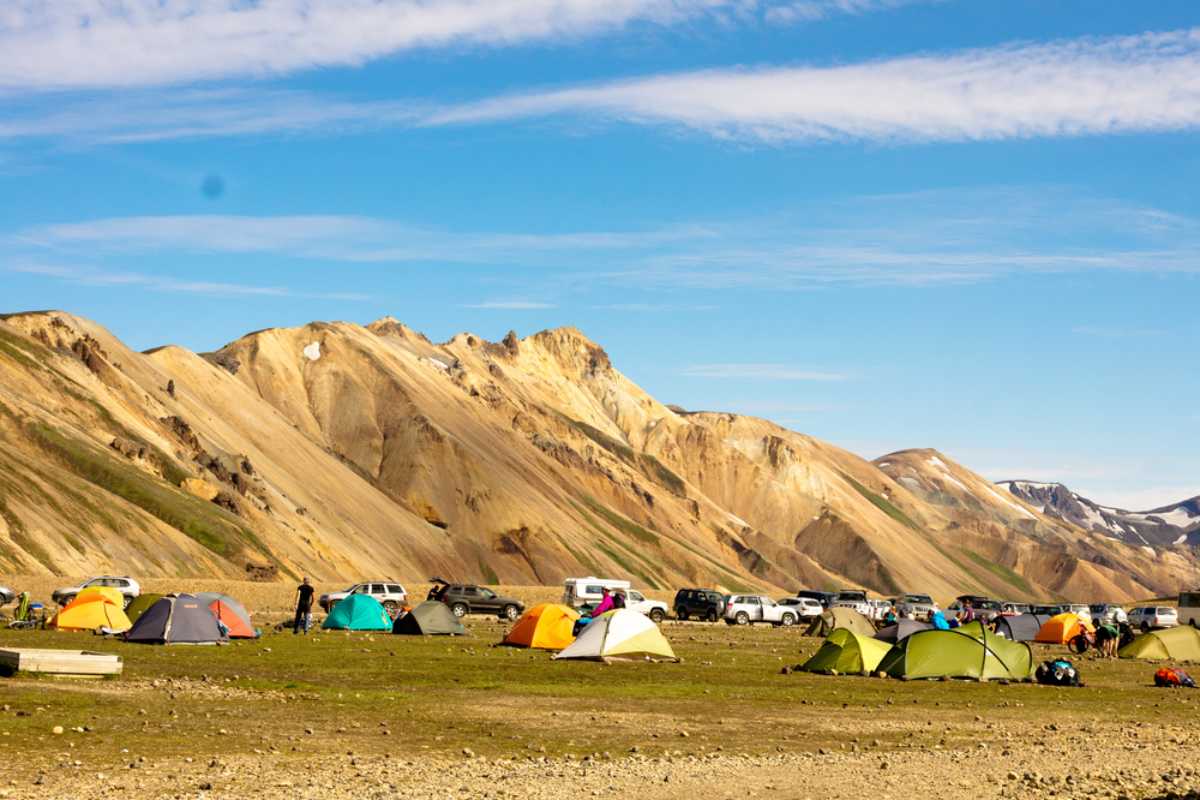 Campingplatz in Island mit Zelten und geparkten Autos in einem offenen Tal unter farbenfrohen Bergen