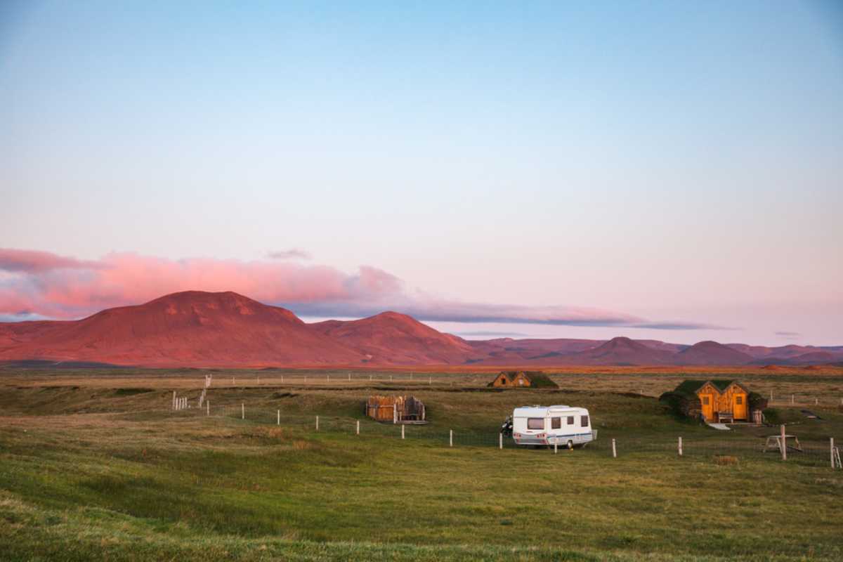 Wohnmobil auf einem ruhigen isl&auml;ndischen Campingplatz bei Sonnenuntergang mit kleinen H&uuml;tten und roten Bergen im Hintergrund