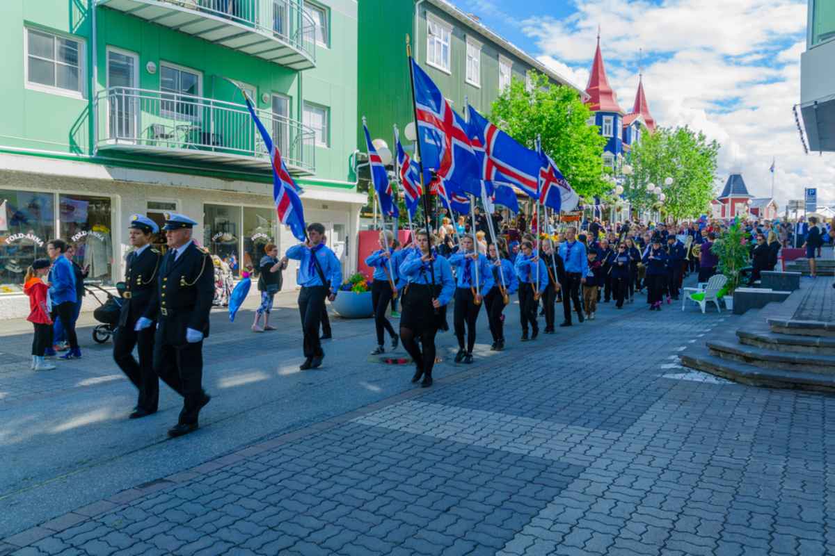 Nationalfeiertagsparade in einer isl&auml;ndischen Stadt mit Menschen, die isl&auml;ndische Flaggen durch die Stra&szlig;e tragen