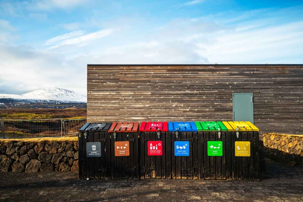 Farblich gekennzeichnete Recycling- und Abfallbeh&auml;lter an einer isl&auml;ndischen Rastst&auml;tte mit Lavafeldern und Bergen im Hintergrund