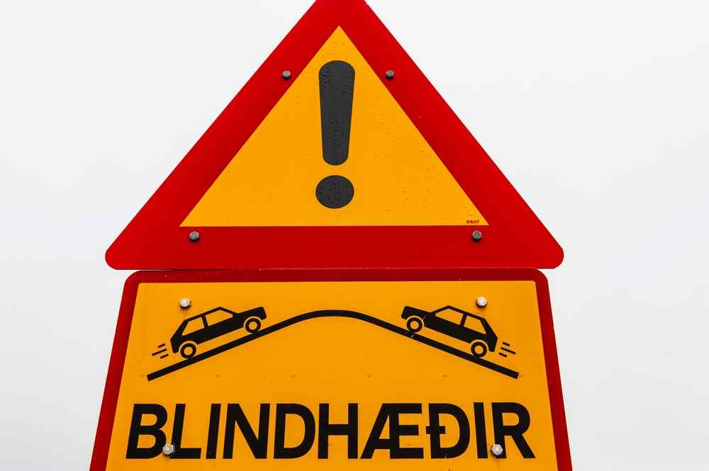 Unterschiede zwischen isländischen Straßenschildern und denen im Rest der Welt Isländisches Schild für eine unübersichtliche Kuppe mit rotem Warndreieck und gelbem Hintergrund.