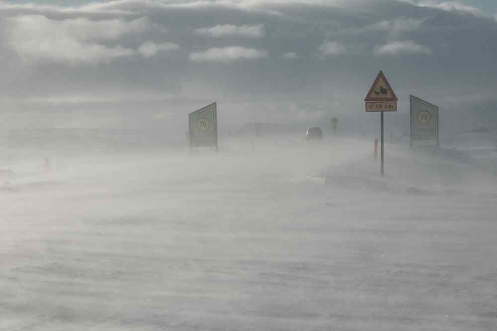 Starke Winde beim Fahren in Island Isländische Straßenschilder, die während eines Schneesturms mit starkem Wind kaum sichtbar sind.