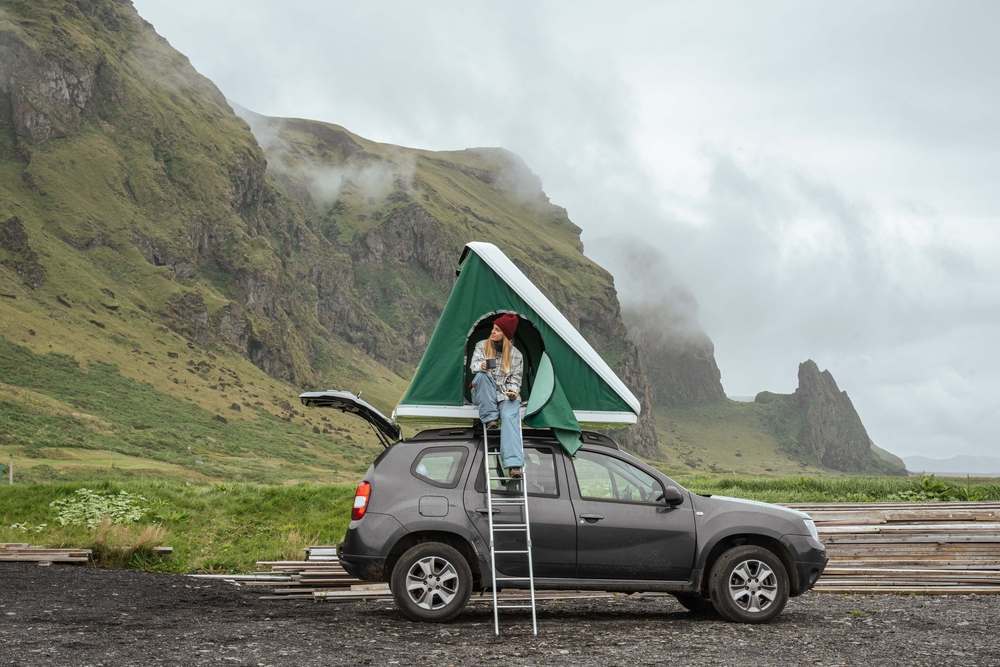 Touristin sitzt oben auf ihrem Camper mit Dachzelt
