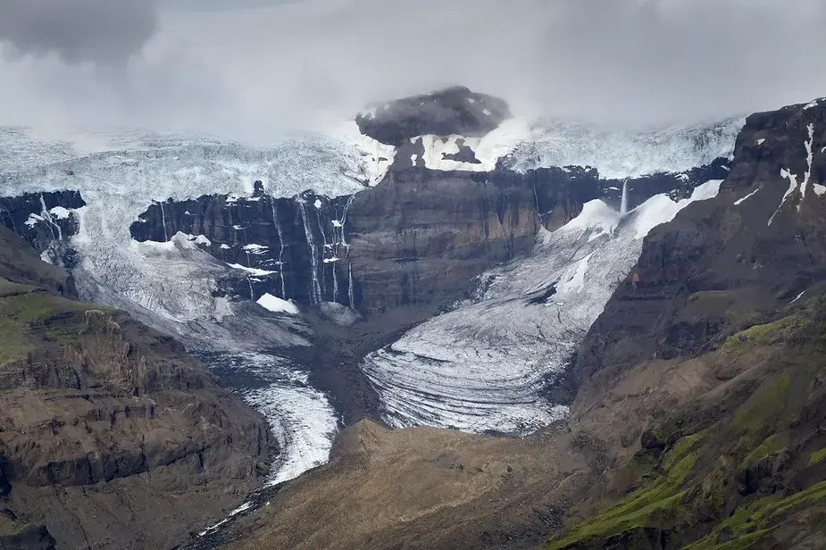 Blick auf den Morsárfoss Wasserfall, der die zerklüfteten Klippen des Vatnajökull-Nationalparks in Island hinabstürzt, umgeben von Gletschern und dram