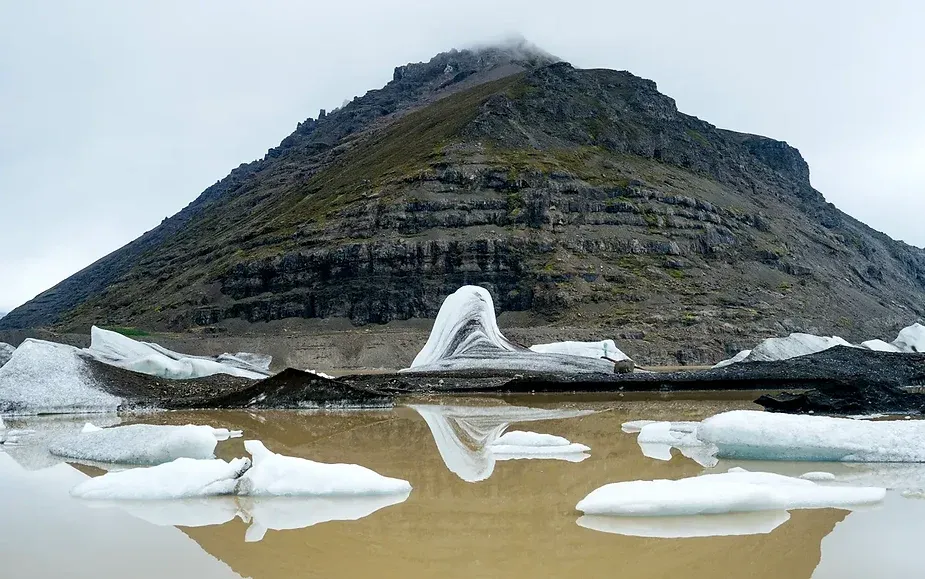 Eisberge in einer Gletscherlagune mit einer raues Berglandschaft im Hintergrund im Vatnaj&ouml;kull-Nationalpark, Island, unter einem bew&ouml;lkten Himmel.
