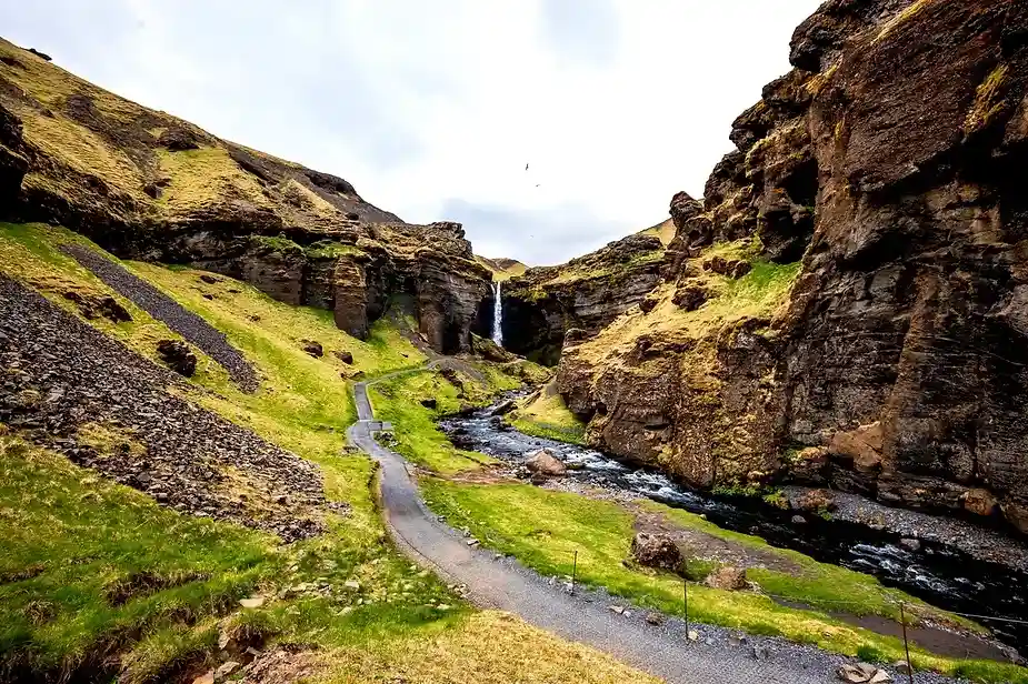 Landschaft des Kvernufoss Wasserfalls mit einem Fluss, der durch ein moosbewachsenes Tal flie&szlig;t.