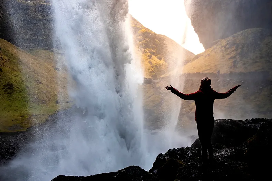 Beeindruckender Blick auf den Kvernufoss Wasserfall mit gr&uuml;nen H&uuml;geln und einem gewundenen Weg, der zum Wasserfall f&uuml;hrt.