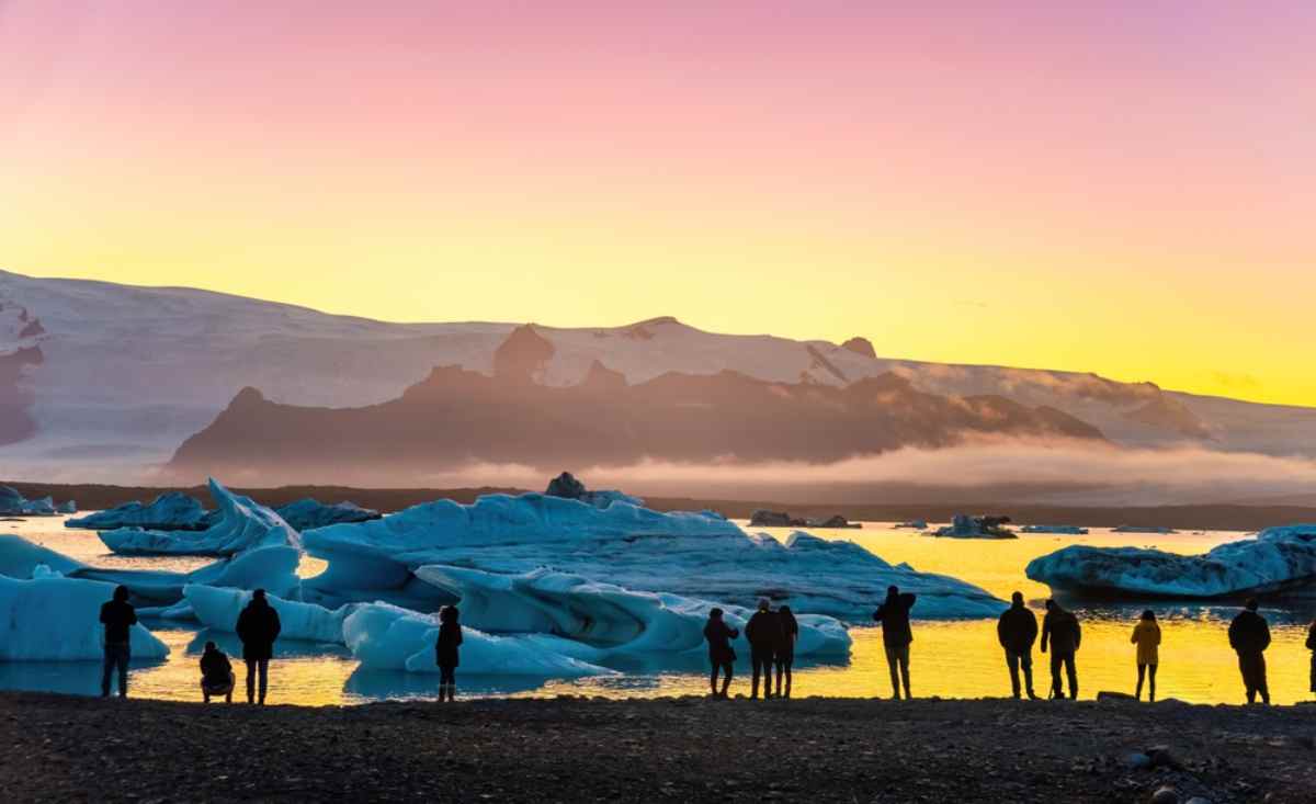 Zwei Touristen in gelber und roter Jacke, Hand in Hand, mit Blick auf die Lagune J&ouml;kulsarlon