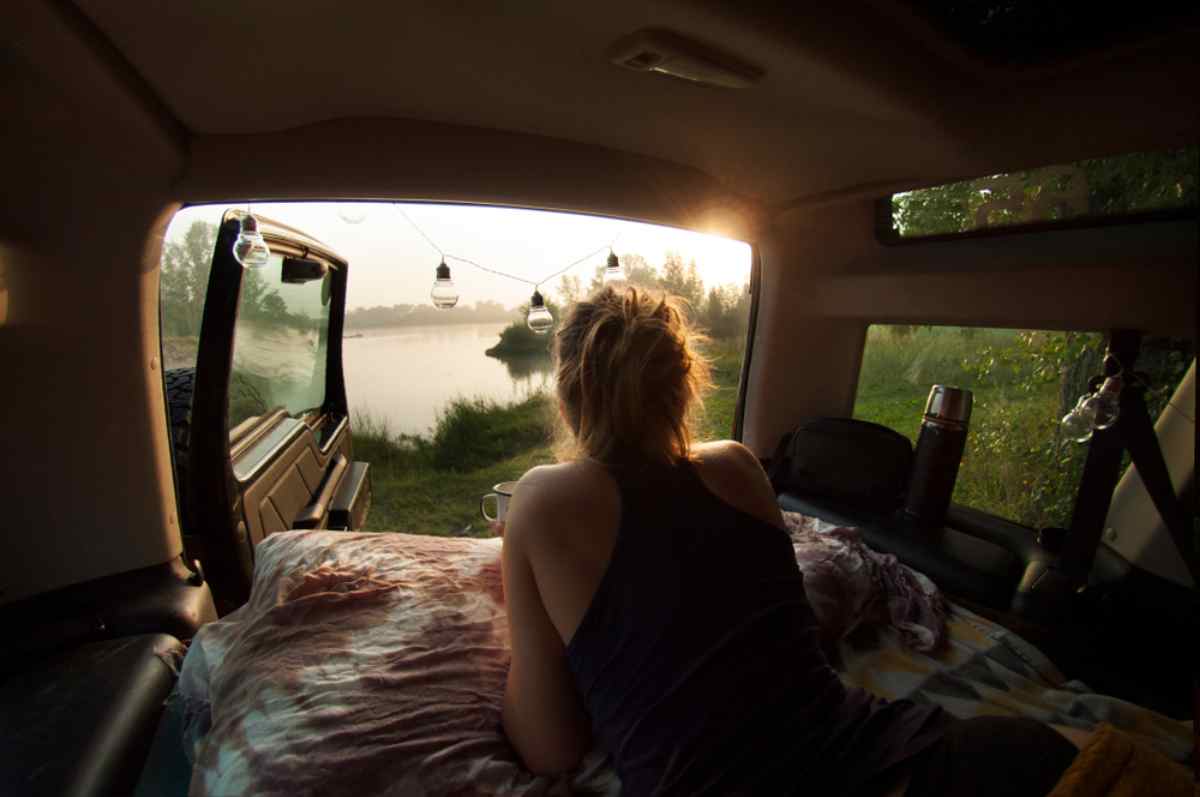 Una mujer disfruta de una taza de café desde el interior de su camper, recostada sobre un colchón de camping.