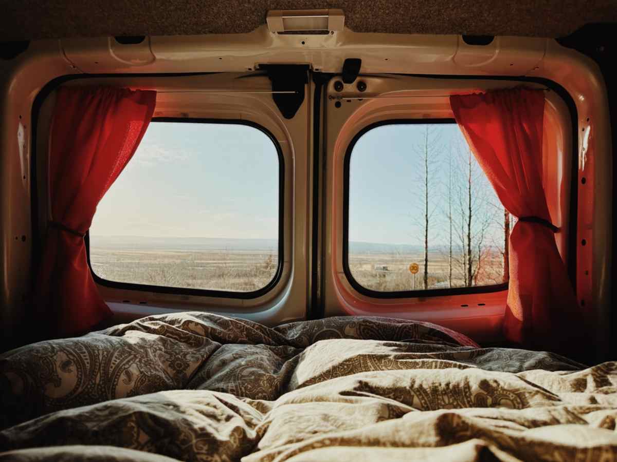 Interior de un camper en su parte trasera donde, a través de sus ventanas, se ve el paisaje primaveral de Islandia en el exterior.