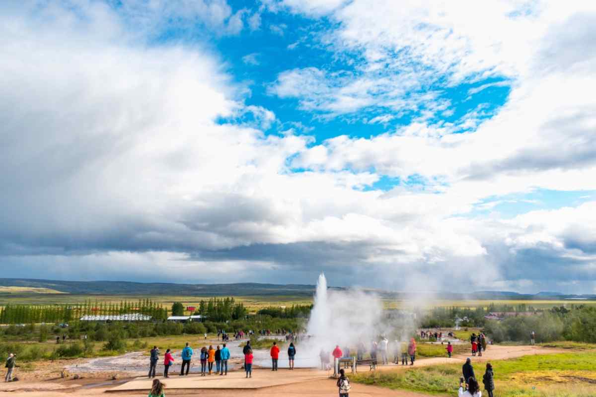 Vista general de la erupción del Geysir islandés mientras, a lo lejos, se ven decenas de personas observándolo.