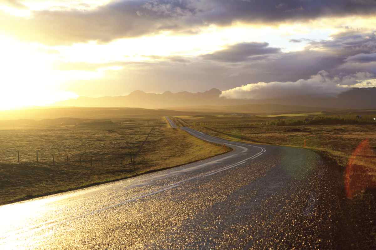 Vista general de una carretera islandesa bañada por el sol con asfalto mojado y brillante.