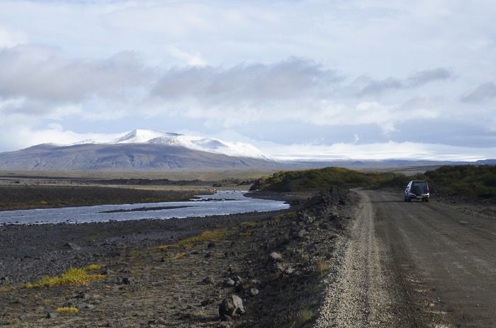 Vista general de un vehículo 4x4 a su paso por una carretera de grava islandesa próxima a lo que parece un río poco caudaloso a la izquierda.